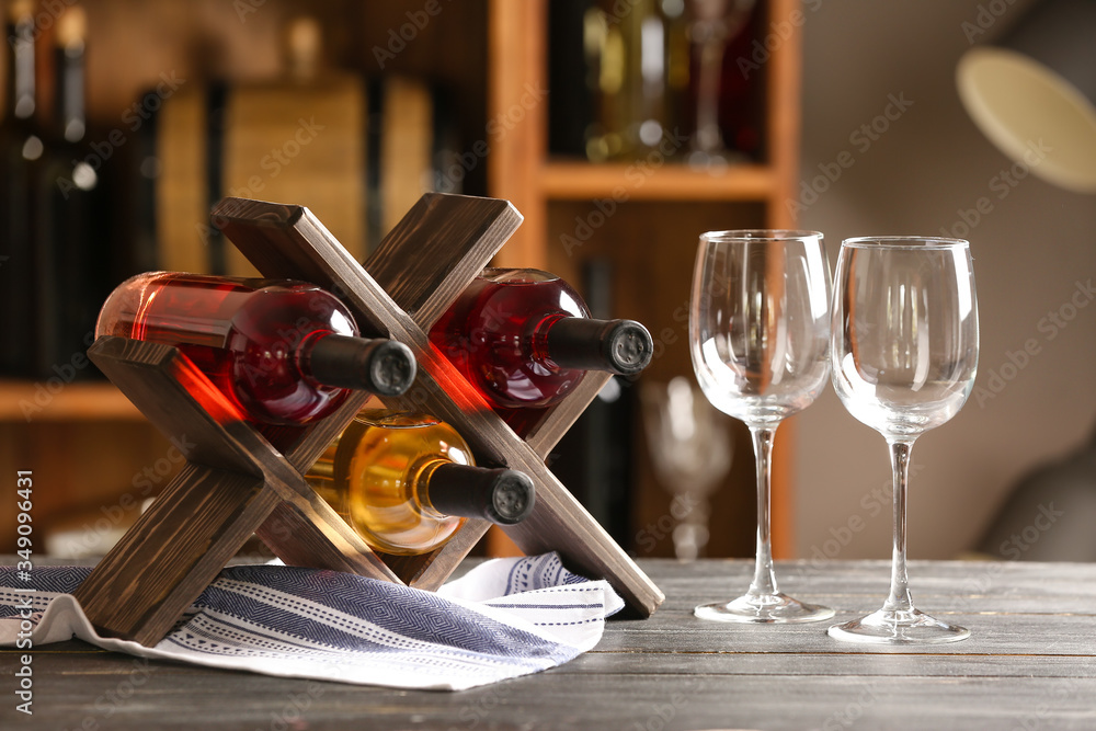 Stand with bottles of wine and glasses on table in cellar