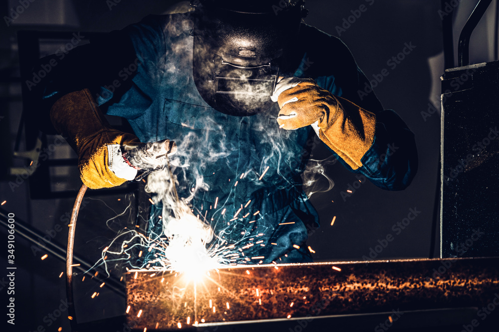 Metal welder working with arc welding machine to weld steel at factory while wearing safety equipmen