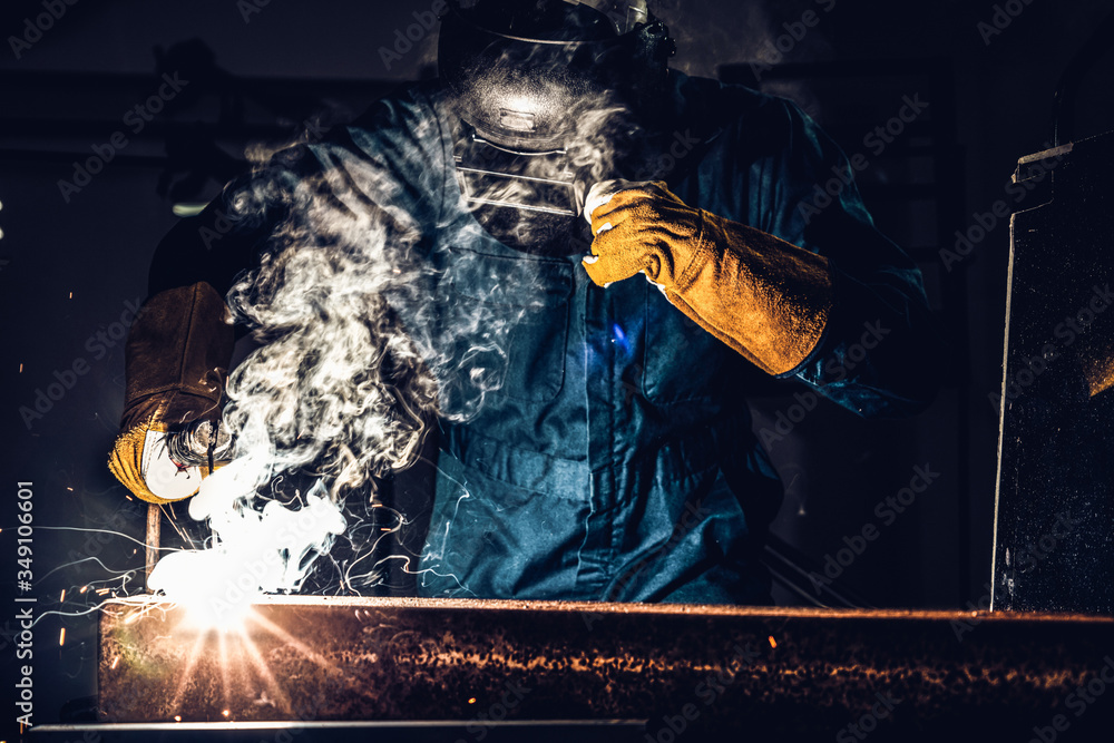 Metal welder working with arc welding machine to weld steel at factory while wearing safety equipmen