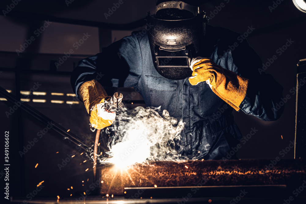 Metal welder working with arc welding machine to weld steel at factory while wearing safety equipmen