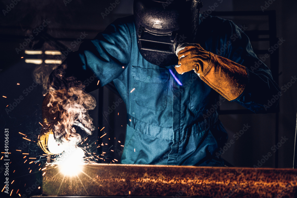 Metal welder working with arc welding machine to weld steel at factory while wearing safety equipmen