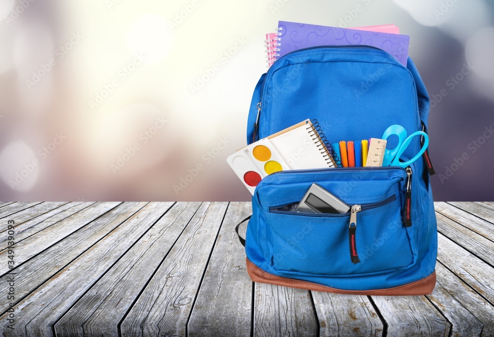 Classic school backpack with colorful school supplies and books on desk.