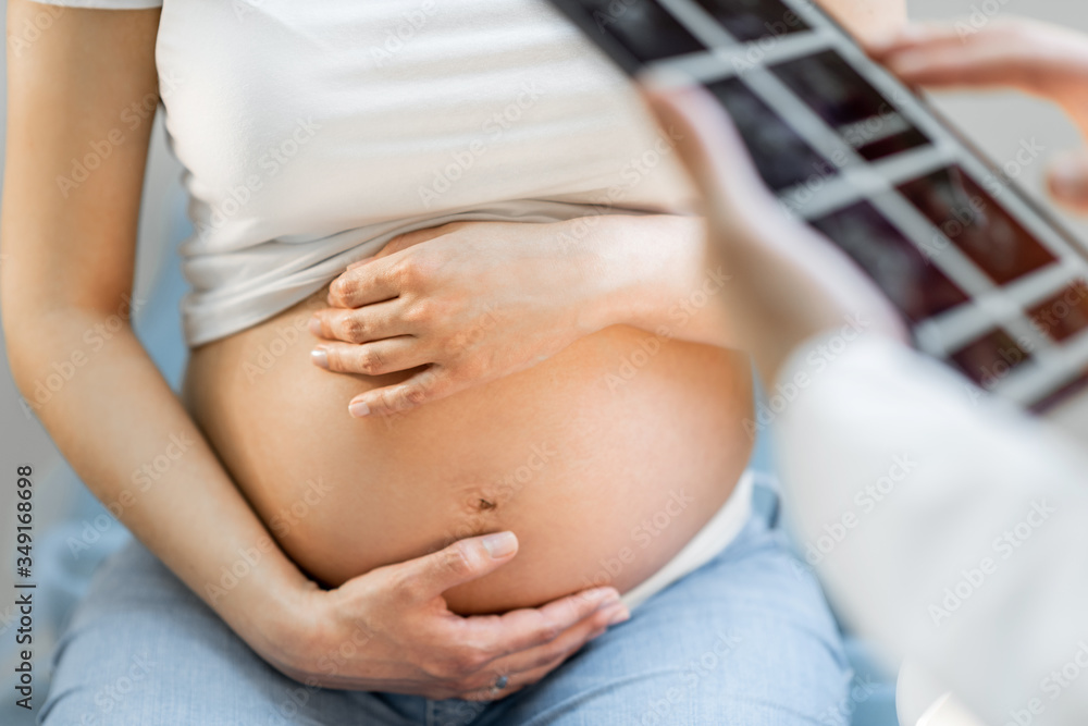 Pregnant woman hugging her belly, sitting on a gynecological chair during a medical examination, cro