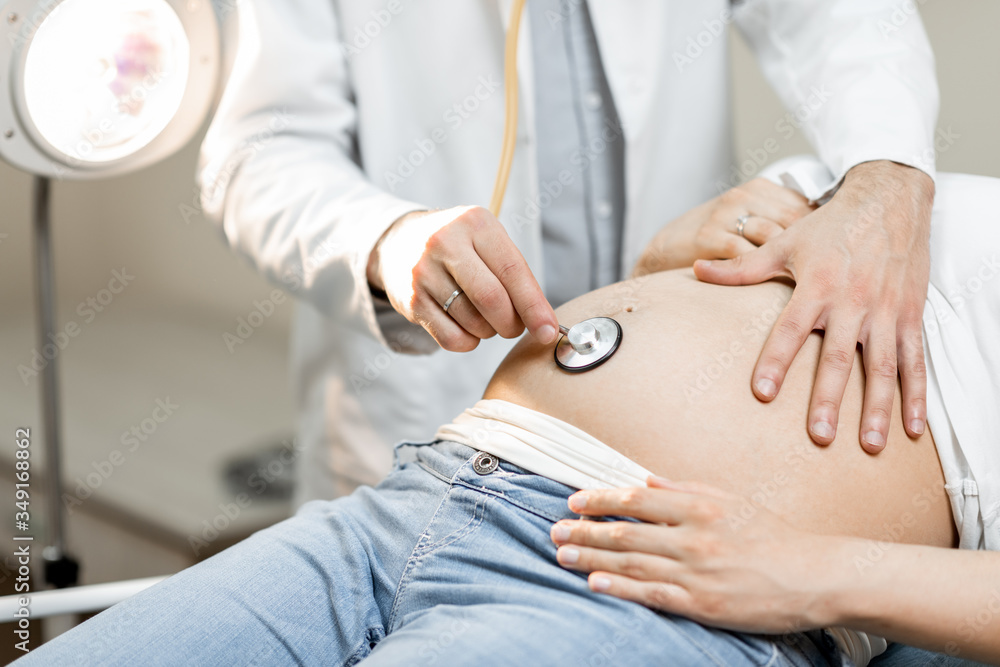 Doctor listening to a pregnant womans belly with a stethoscope during a medical examination, close-