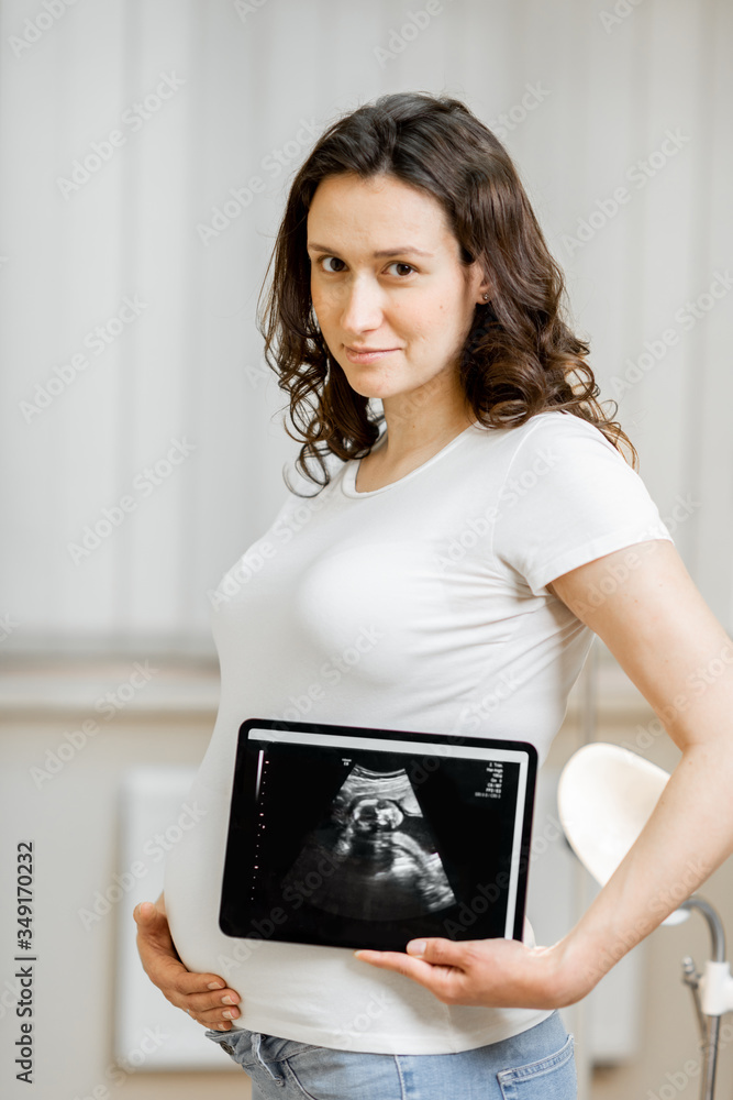 Portrait of a beautiful pregnant woman holding digital tablet with an ultrasound scan of her unborn 