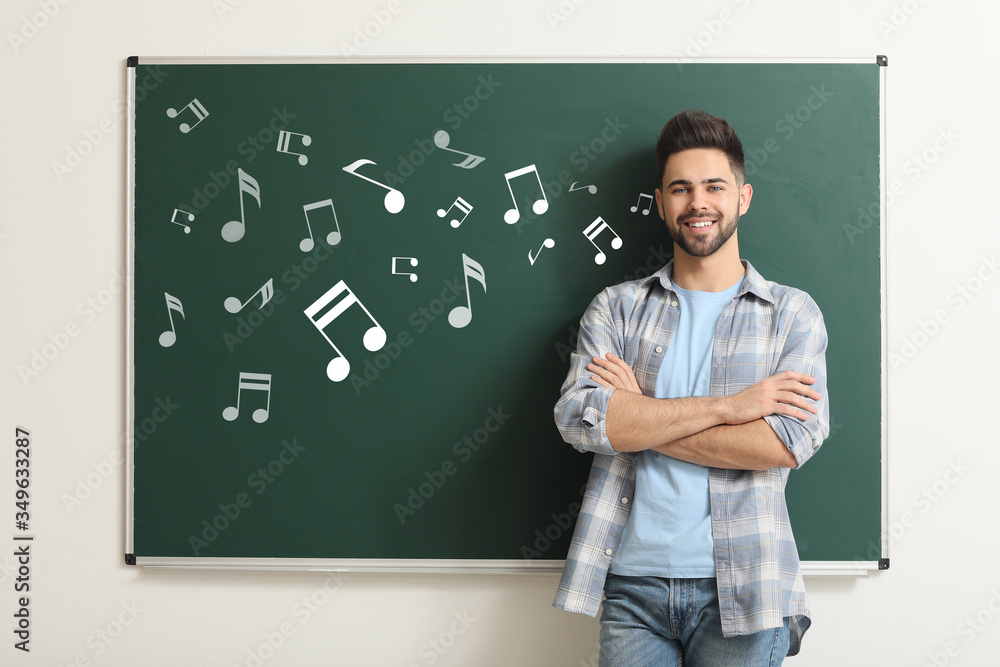 Handsome music teacher near blackboard in classroom