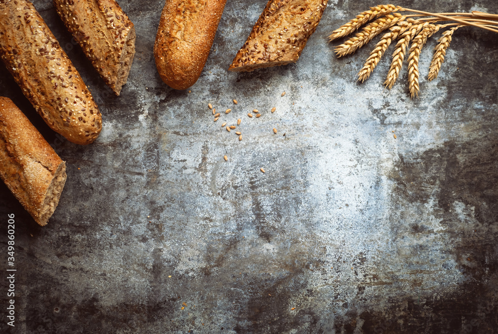 Fresh bakery food. Crusty loaves of mixed breads and buns and ears of wheat on rustic table backgrou