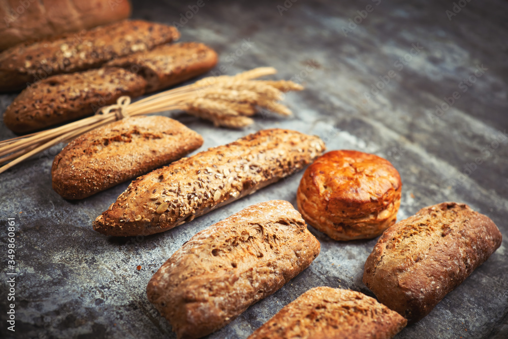 Fresh bakery food. Crusty loaves of mixed breads and buns and ears of wheat on rustic table backgrou