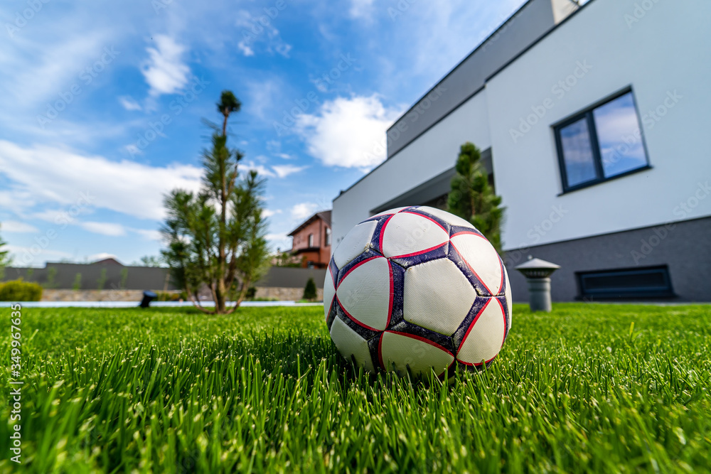 Ball on green lawn. Modern out-to-date house background. Blue sky above. Nobody in the yard. Modern 