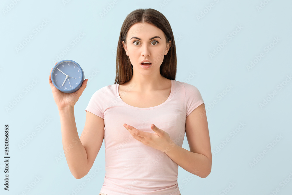 Shocked young woman with alarm clock on color background