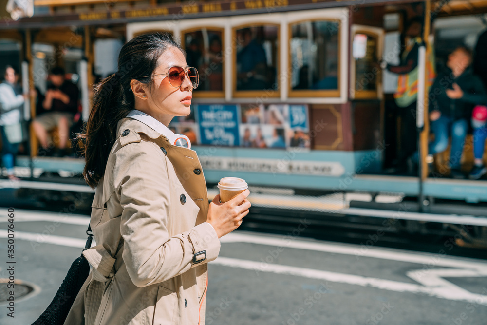 Young woman standing on street drinking coffee to go while putting headphones on neck. beautiful ele