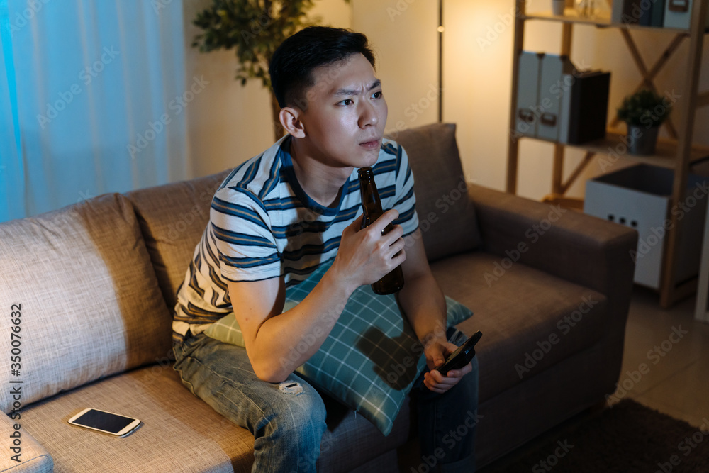 frowning young man concentrated watching sports on TV in dark living room at home. handsome guy worr