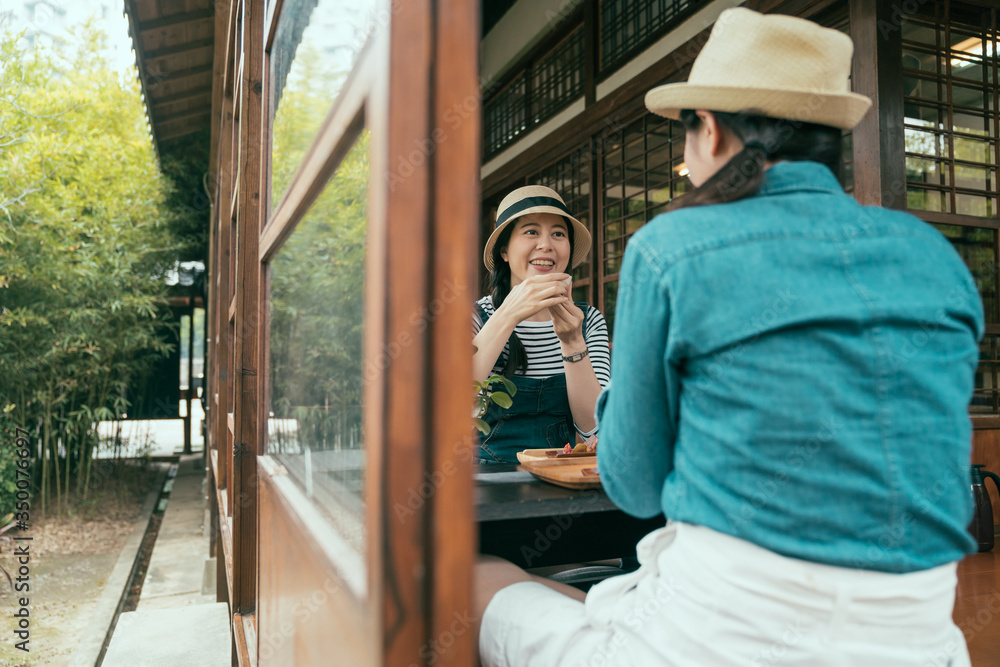 shot from outdoor through window and door with two asian girl friends sitting on wooden floor in ryo