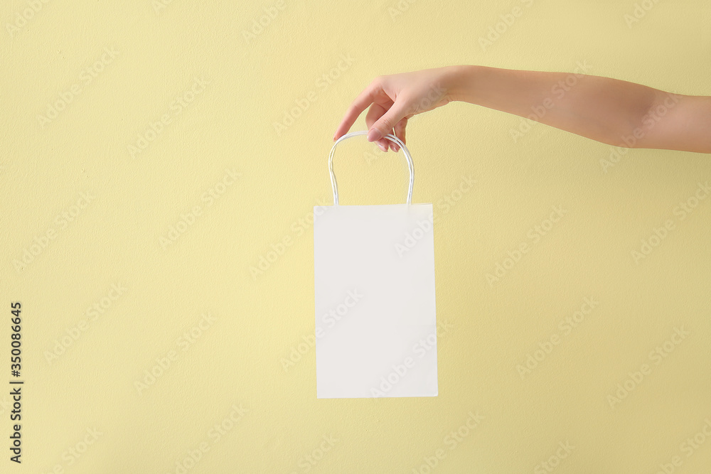 Hand with paper bag on color background