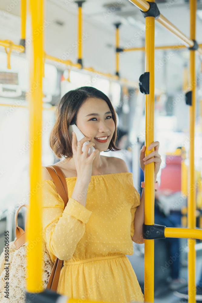 Young Asian attractive woman standing on the bus and using phone.