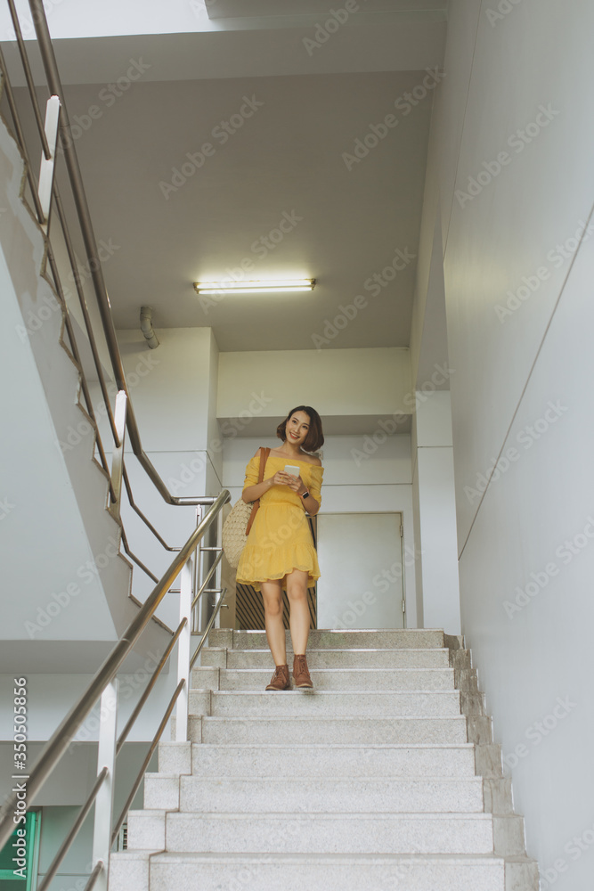 Young Asian woman going down stairs and texting on her phone.