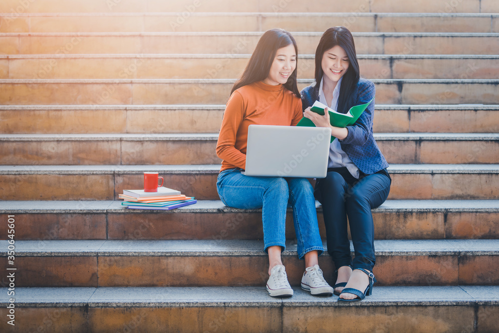 大学里坐在楼梯上使用笔记本电脑的多元化青少年。微笑的亚洲女性