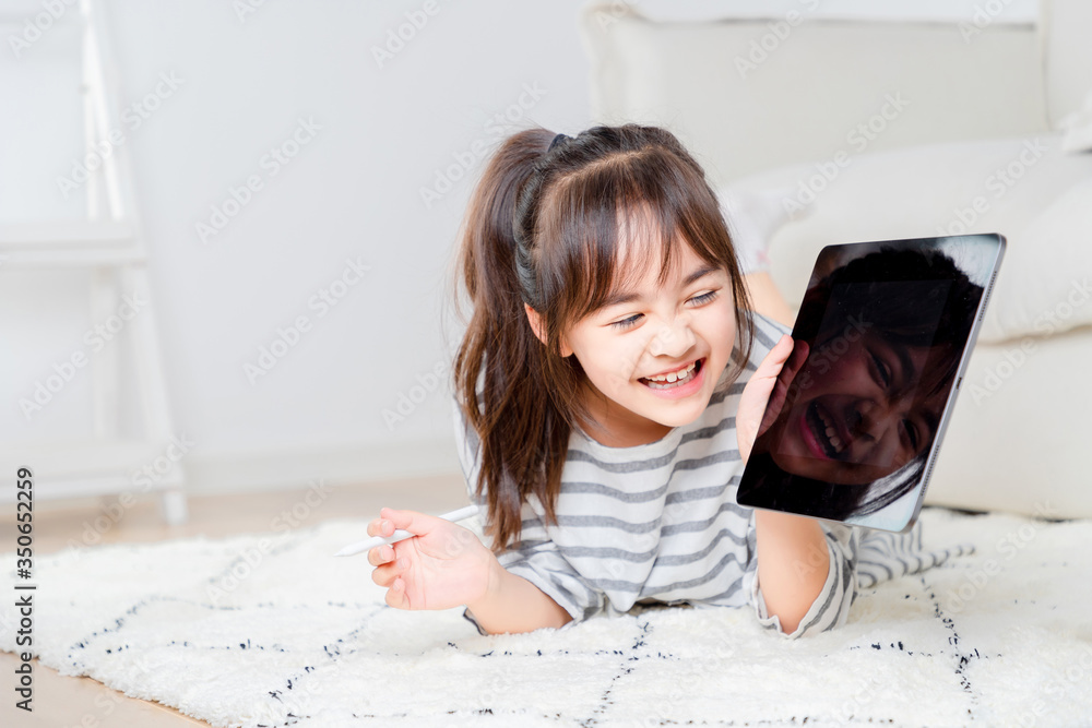 Asian little girl playing tablet on the carpet