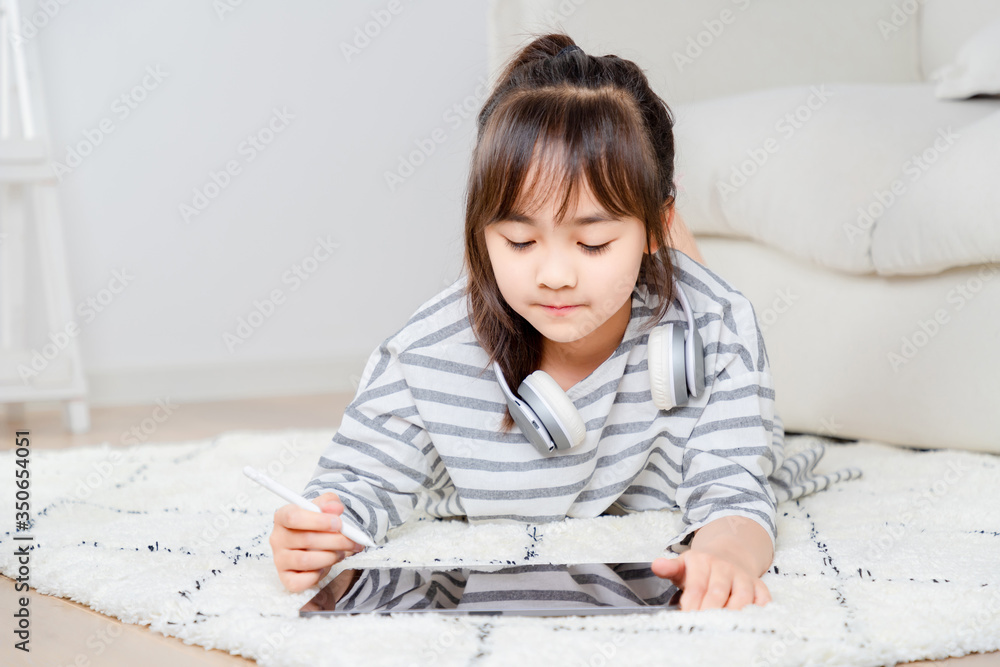 Asian little girl playing tablet on the carpet