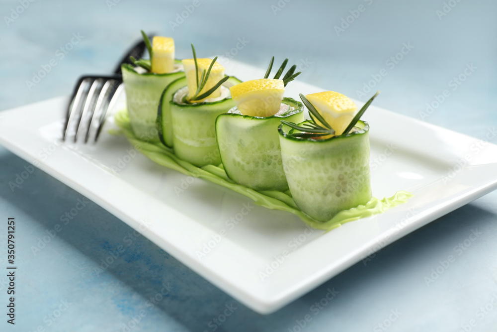 Plate with tasty cucumber rolls on color background