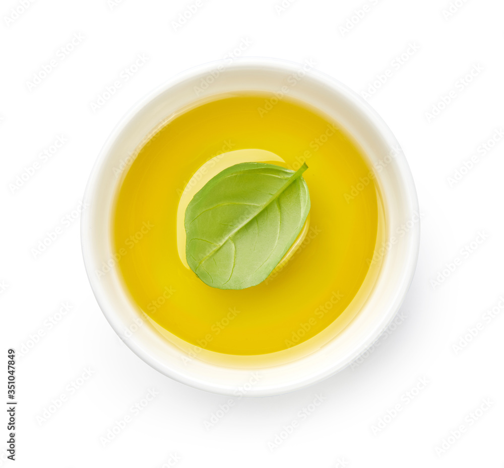 Olive or vegetable oil in white bowl. Top view of oil with basil leaf isolated on white background.