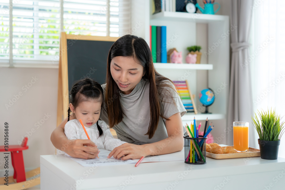 亚洲幼儿园女孩与母亲在家用彩色铅笔在书中画画，家