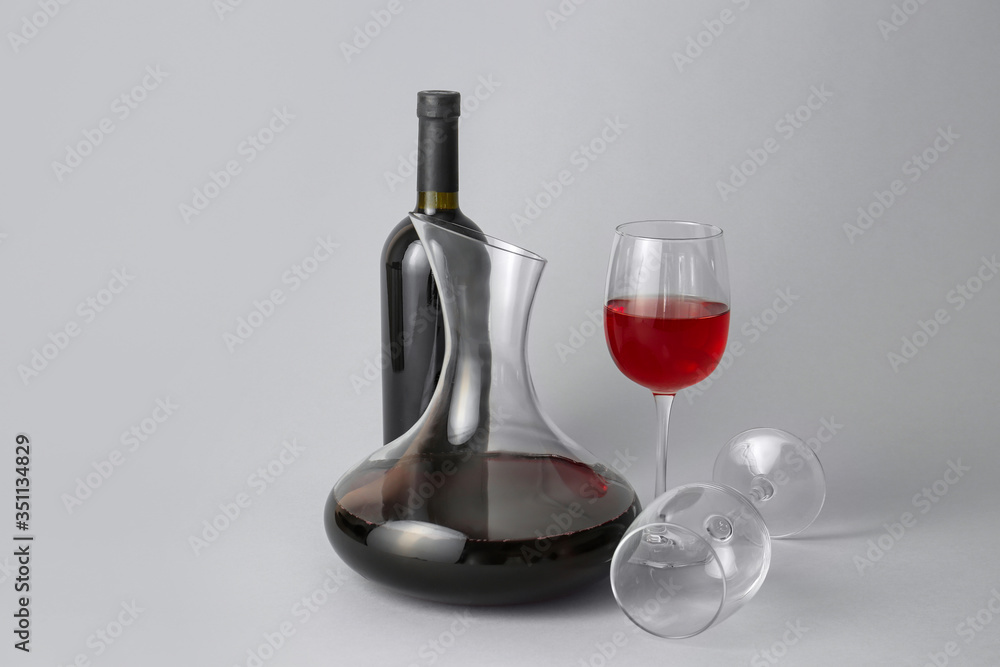 Decanter and bottle of wine with glasses on grey background