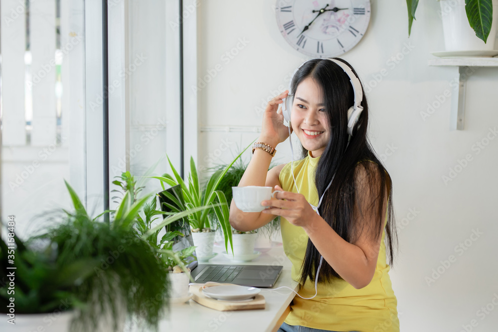 亚洲微笑女生戴无线耳机在咖啡店与skype老师在线学习，