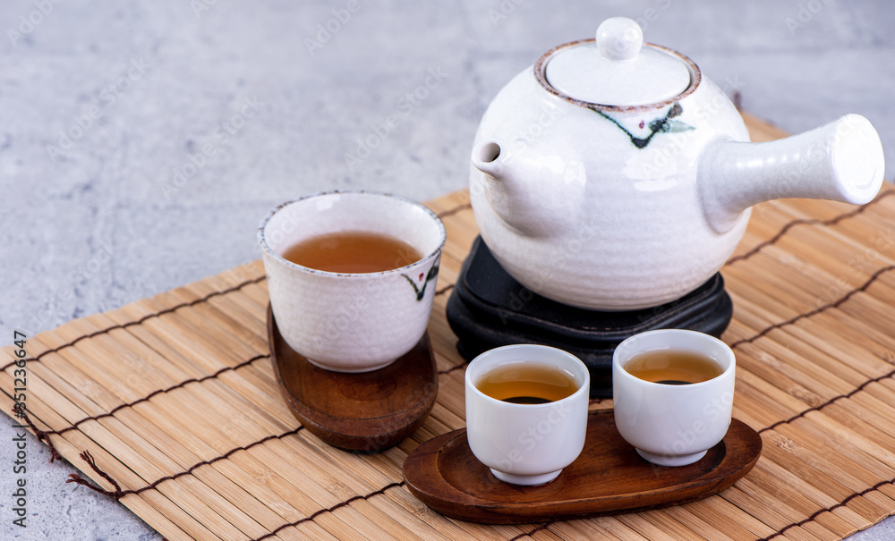 Hot tea in white teapot and cups on a sieve over bright gray cement background, closeup, copy space 