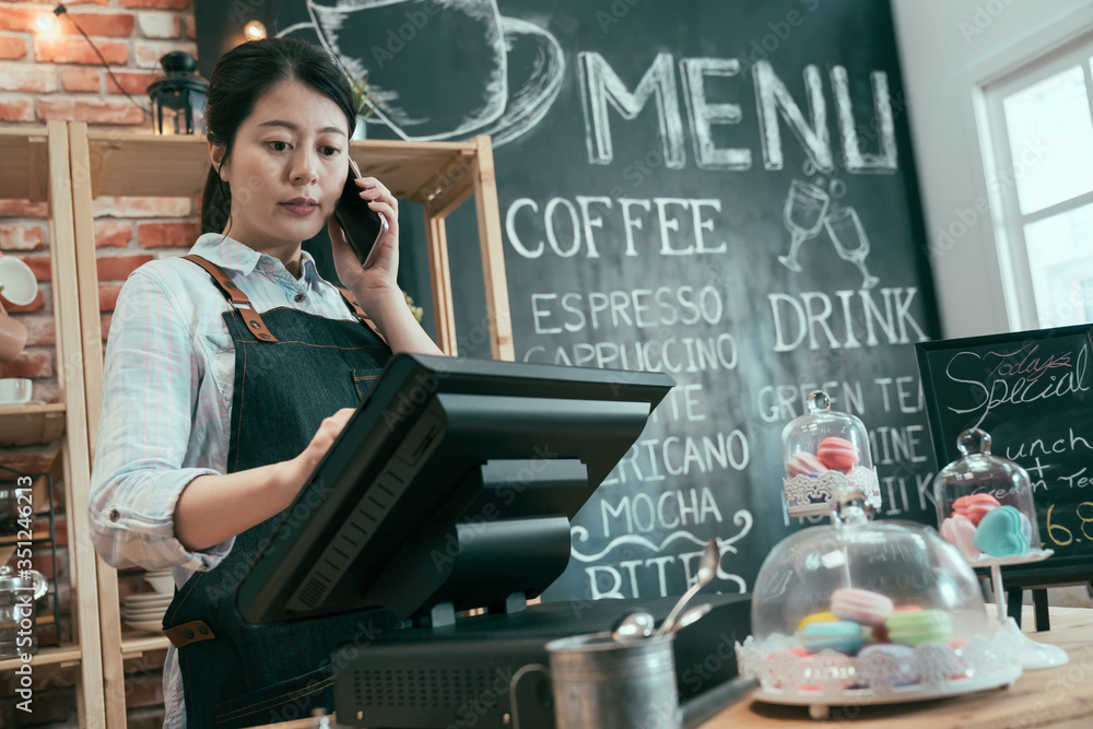 年轻的亚裔日本女店员在咖啡店工作。女服务员在顾客面前打手机