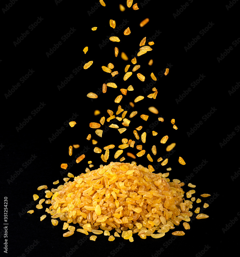 Falling dry bulgur wheat grains isolated on black background