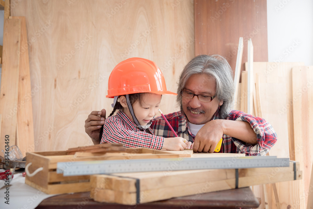 Senior male asian carpenter and grandchild making wooden house at home . Little asian girl working a