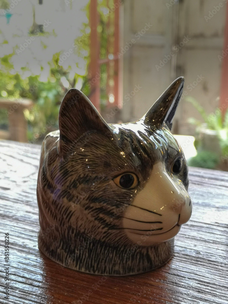 The gray cat head is ceramics placed on a wooden table, the background is blurred.