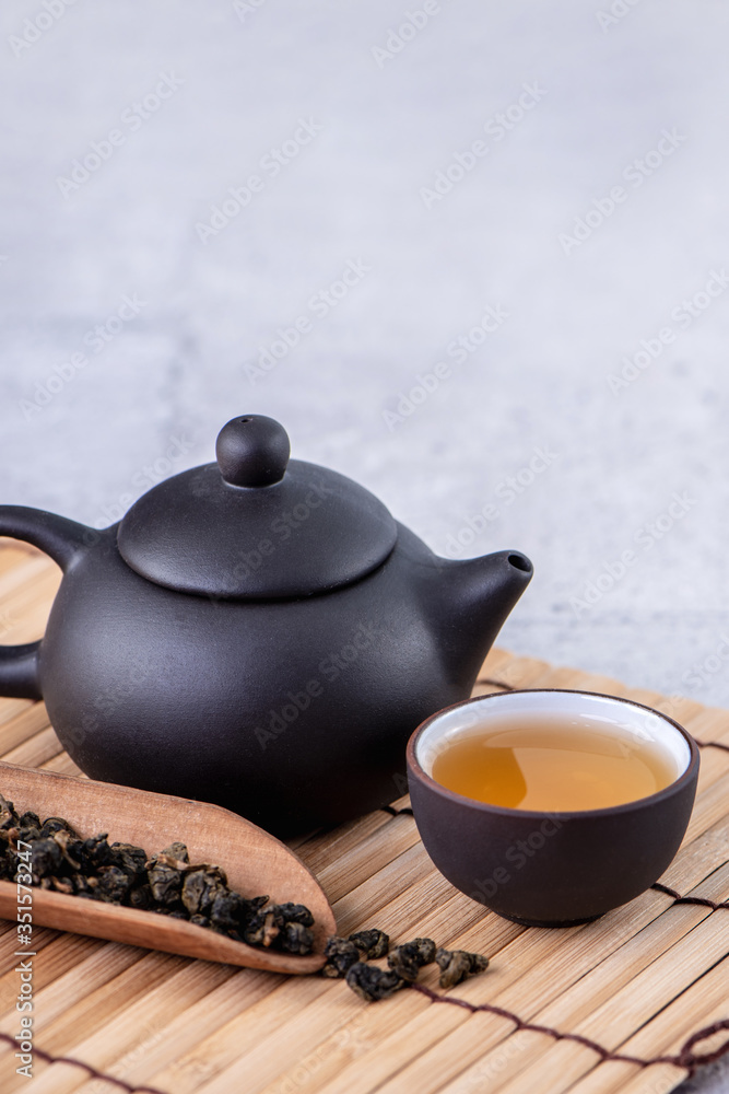 Hot tea in black teapot and cups and dry tea leaves over bright gray cement background, close up, co