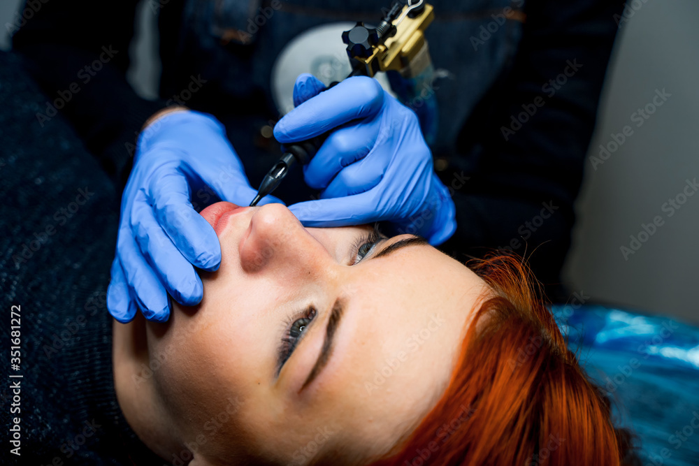 Young woman having permanent makeup on lips in beauty salon. Close up