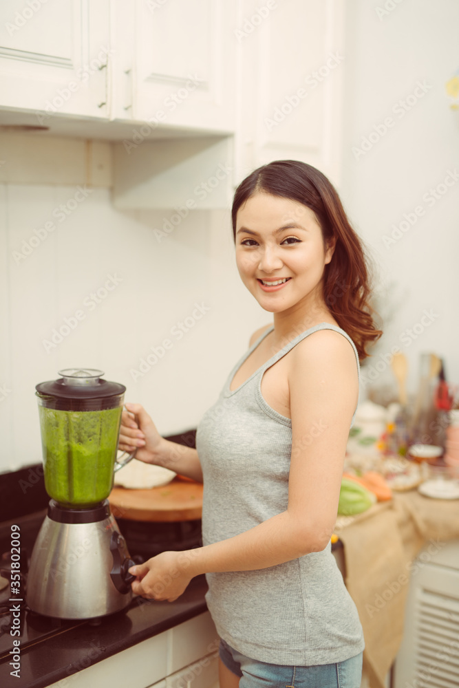 蔬菜奶昔女士在厨房里用搅拌机搅拌绿色奶昔