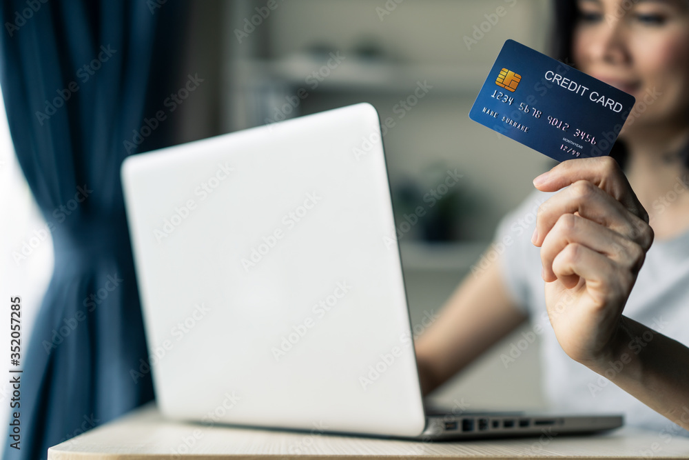 Young beautiful Asian woman holding credit card shopping online from home. Girl using laptop compute