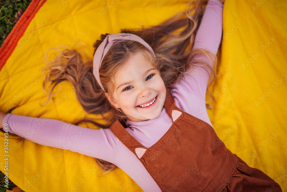 Portrait of a gorgeous smiling little girl lying on yellow blanket.