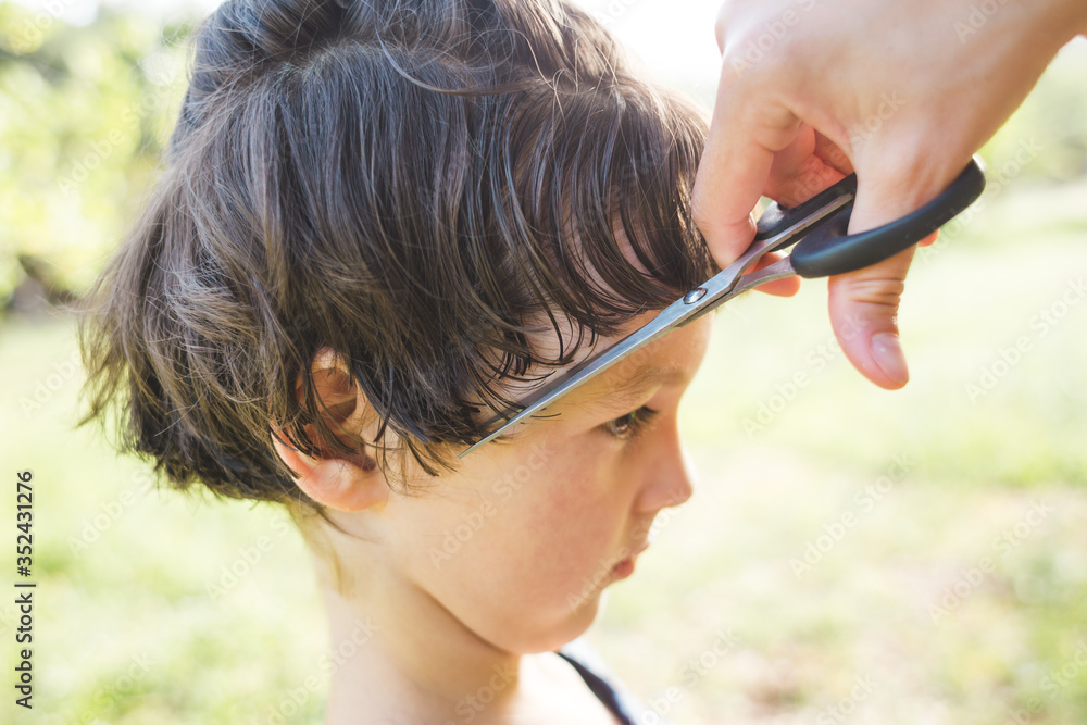 Boy with a new haircut, A woman cuts the hair of a child in the yard of the house during quarantine.