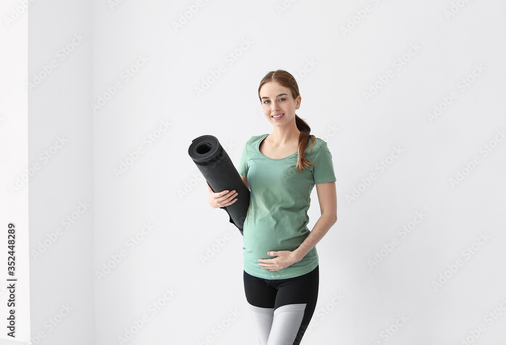 Young pregnant woman with yoga mat in gym