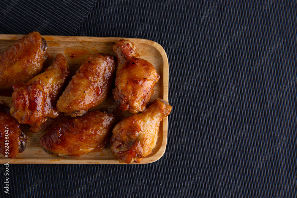 Baked chicken wings in a wooden dish on a dark cloth.