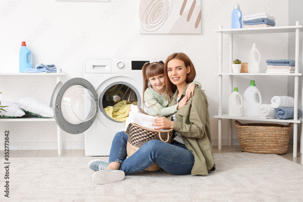 Woman and her cute little daughter doing laundry at home