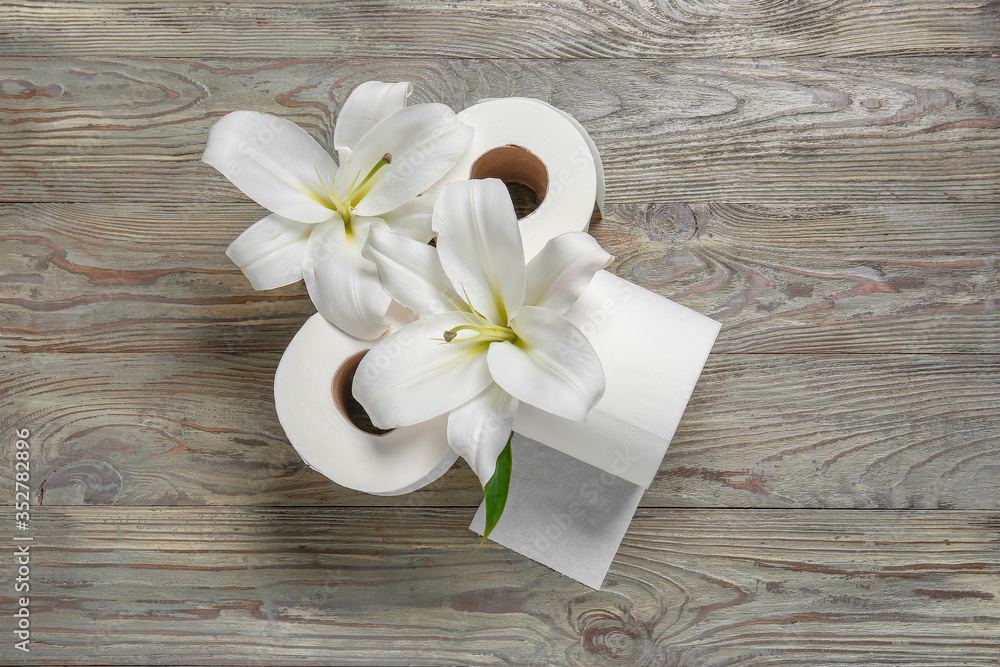 Rolls of toilet paper and flowers on wooden background