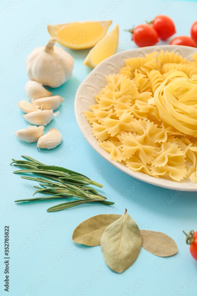 Plate with different uncooked pasta and products on color background