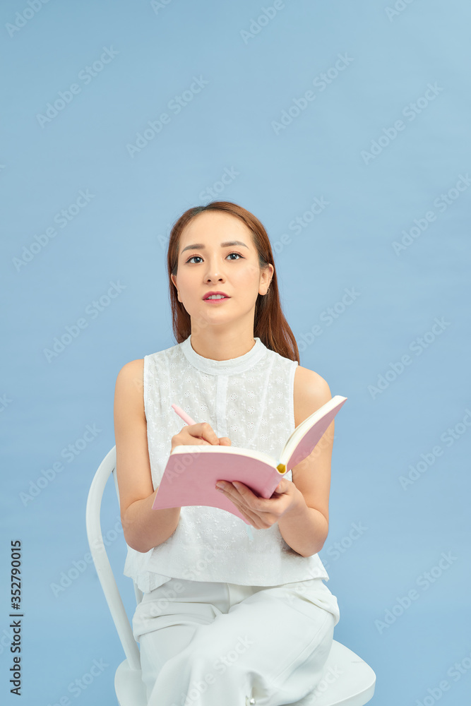 Smiling lovely girl writing in a diary while sitting on a chair