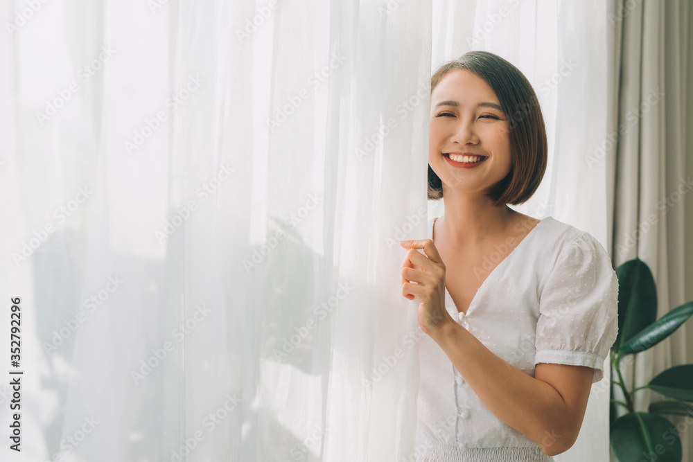 一个幸福的女人打开窗帘，在温暖的光线下享受新的一天的侧视图