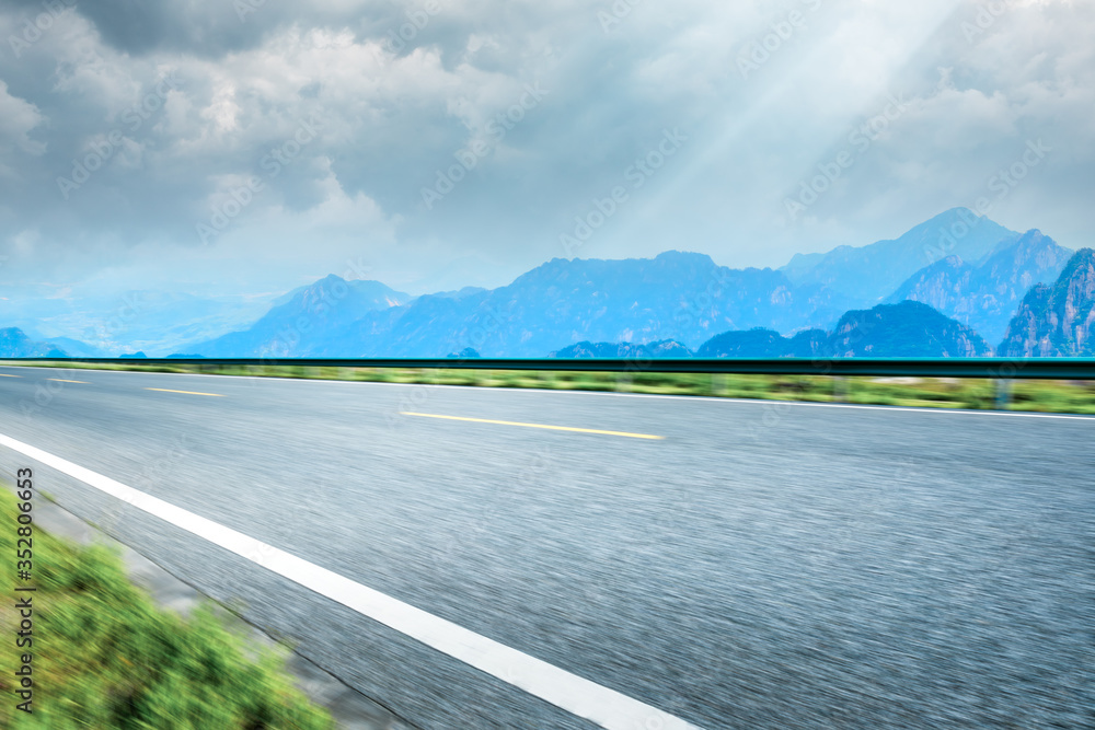 Motion blurred asphalt road and green mountain,road ground background.