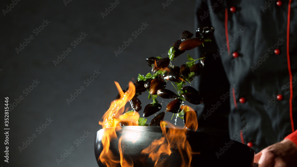 Closeup of chef throwing mussels from wok