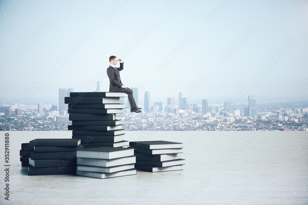 Businessman in suit sitting on book pile.