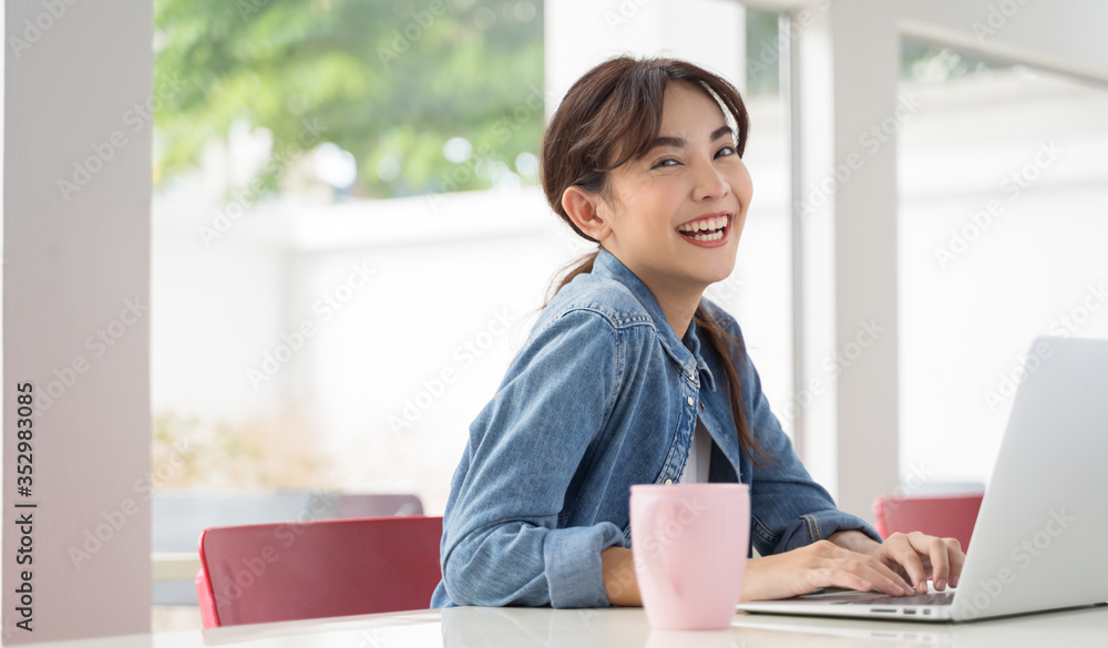 亚洲女孩拿着笔记本电脑在咖啡店工作女人开心地笑着